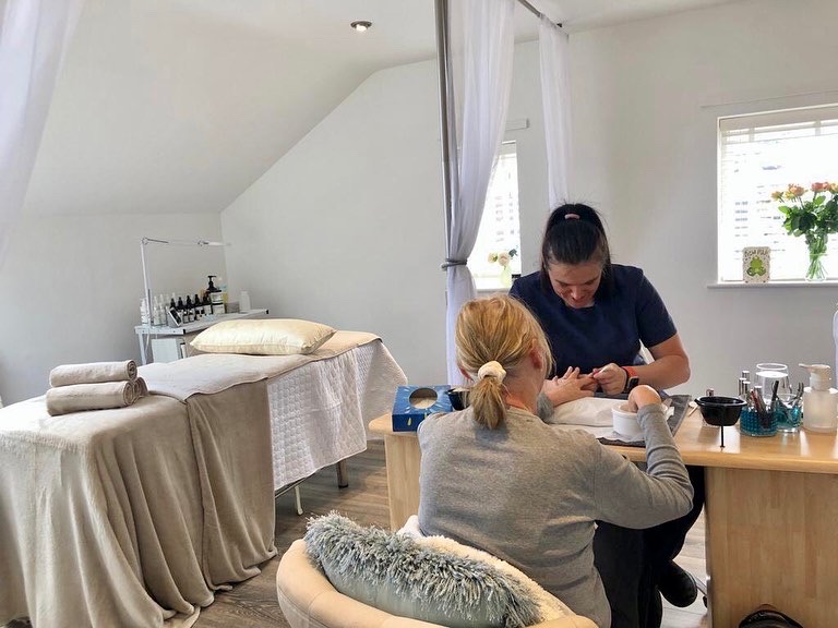 A beauty therapist caring for a client's nails beside the salon's bright windows